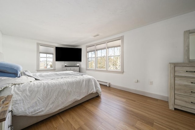 bedroom with a baseboard radiator, baseboards, visible vents, and wood finished floors