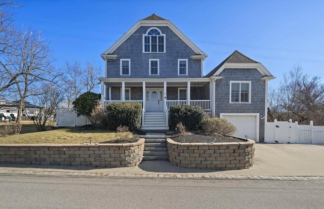 shingle-style home featuring a gate, fence, a porch, concrete driveway, and a garage