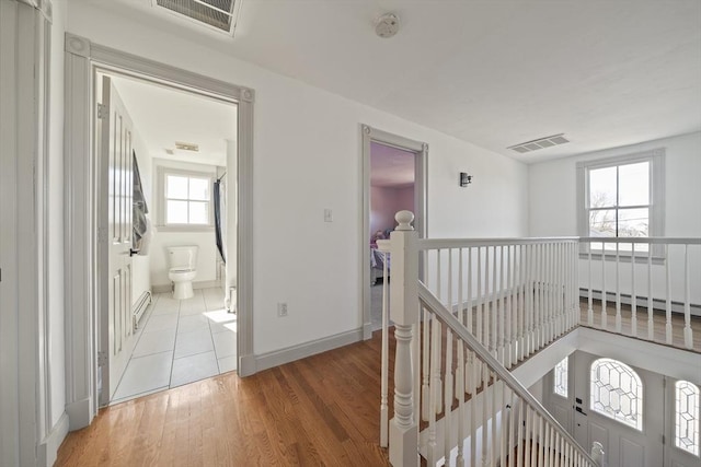 hallway with light wood-style flooring, an upstairs landing, visible vents, and baseboards