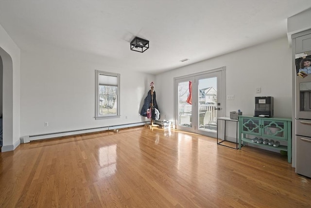 interior space with arched walkways, baseboard heating, a healthy amount of sunlight, and wood finished floors