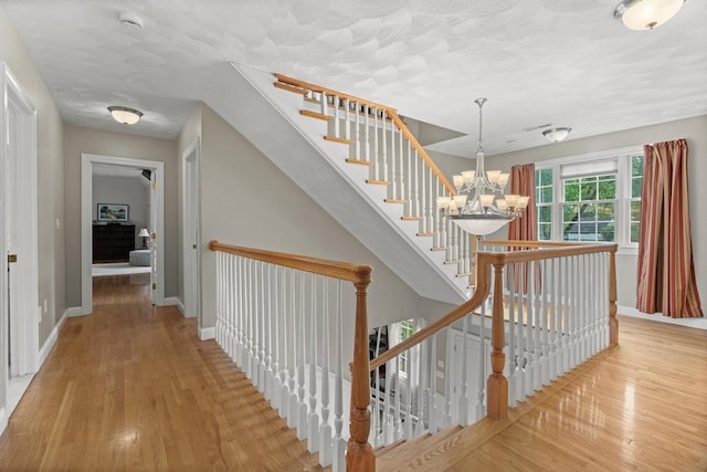 staircase with a chandelier, hardwood / wood-style flooring, baseboards, and a textured ceiling