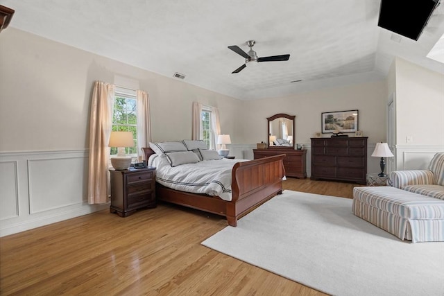 bedroom with a decorative wall, light wood finished floors, a wainscoted wall, and ceiling fan