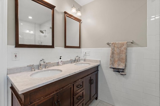 bathroom with tile walls, double vanity, tiled shower, and wainscoting