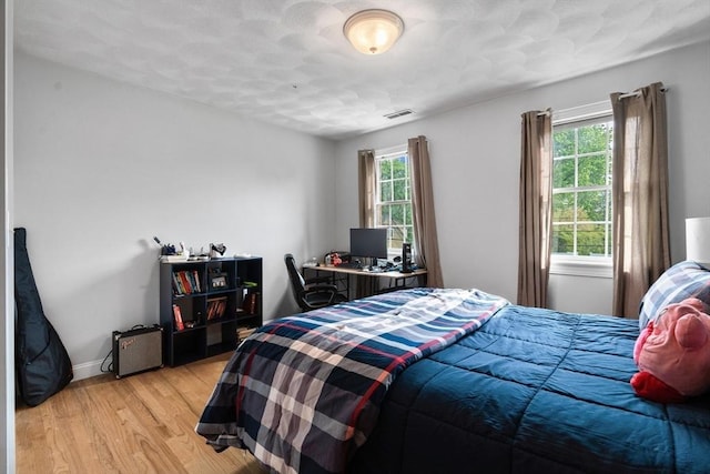 bedroom with multiple windows, light wood-type flooring, and baseboards