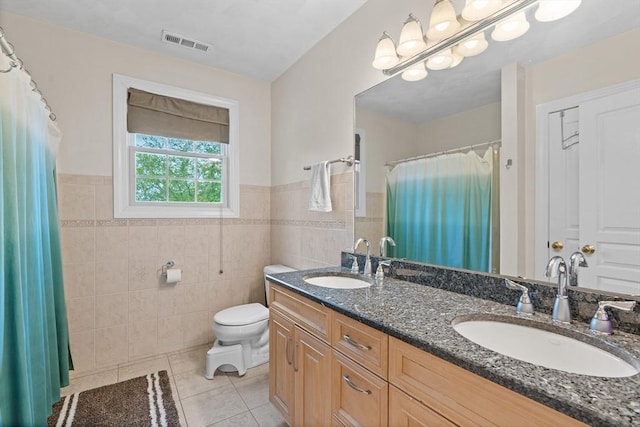 full bath featuring tile walls, tile patterned flooring, toilet, wainscoting, and double vanity