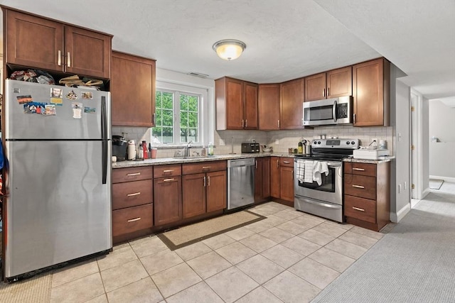 kitchen featuring stainless steel appliances, a sink, backsplash, light stone counters, and light tile patterned floors