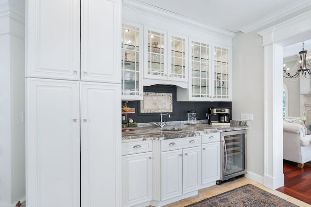 bar area featuring wine cooler, light wood-type flooring, ornamental molding, a sink, and a chandelier