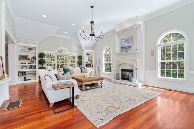 living room with a chandelier, wood finished floors, a lit fireplace, wainscoting, and crown molding