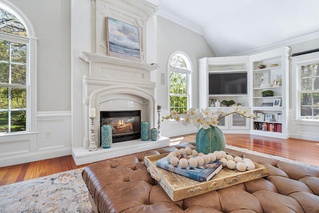 living area featuring wood finished floors, lofted ceiling, a wainscoted wall, a glass covered fireplace, and crown molding