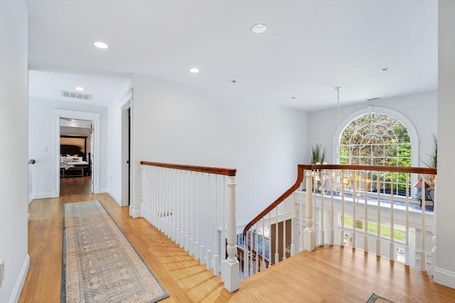 hall with an upstairs landing, wood finished floors, and recessed lighting