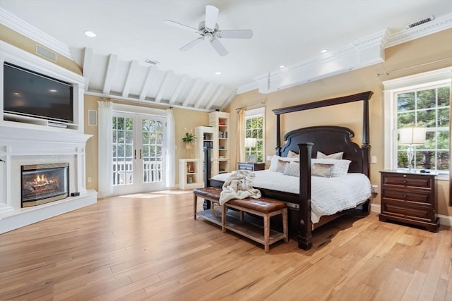 bedroom featuring light wood finished floors, multiple windows, a glass covered fireplace, ornamental molding, and lofted ceiling