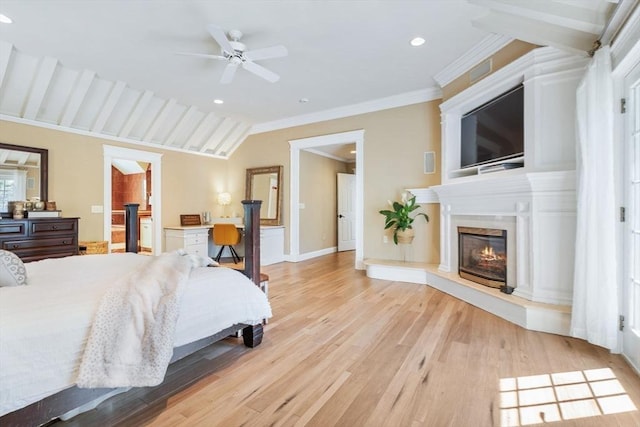 bedroom with a glass covered fireplace, light wood-type flooring, ornamental molding, baseboards, and vaulted ceiling