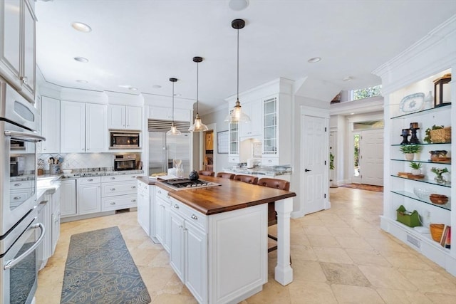 kitchen featuring built in appliances, wooden counters, backsplash, white cabinets, and ornamental molding