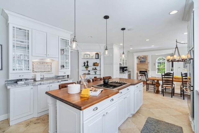 kitchen featuring stainless steel gas stovetop, white cabinets, a kitchen island, glass insert cabinets, and a fireplace