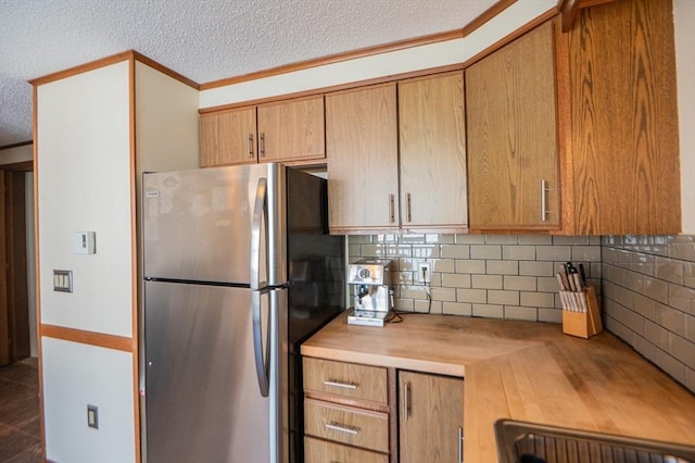 kitchen with tasteful backsplash, brown cabinets, freestanding refrigerator, a textured ceiling, and crown molding
