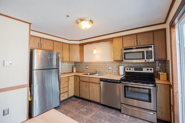kitchen with a sink, stainless steel appliances, ornamental molding, light countertops, and decorative backsplash