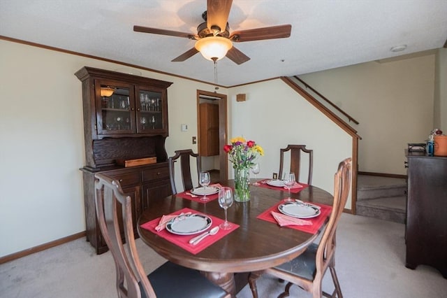 dining room with crown molding, light carpet, baseboards, and a ceiling fan