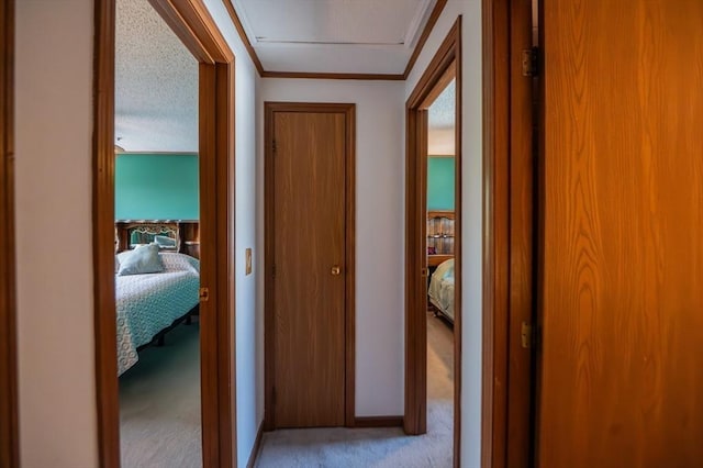 hallway with ornamental molding, light carpet, attic access, and baseboards
