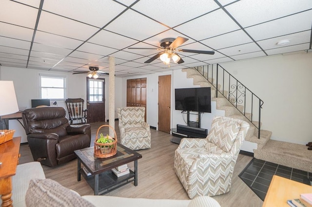 living room with stairs, a drop ceiling, ceiling fan, and wood finished floors