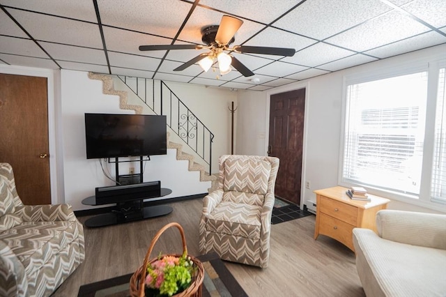 living room with a paneled ceiling, wood finished floors, a ceiling fan, and stairs