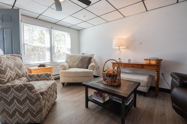 living area featuring a drop ceiling, baseboard heating, baseboards, ceiling fan, and wood finished floors