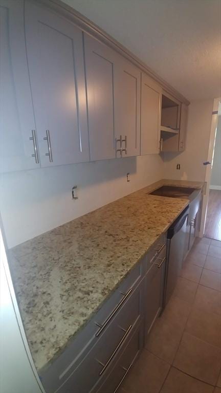 kitchen featuring dishwasher, light tile patterned floors, light stone counters, and gray cabinetry