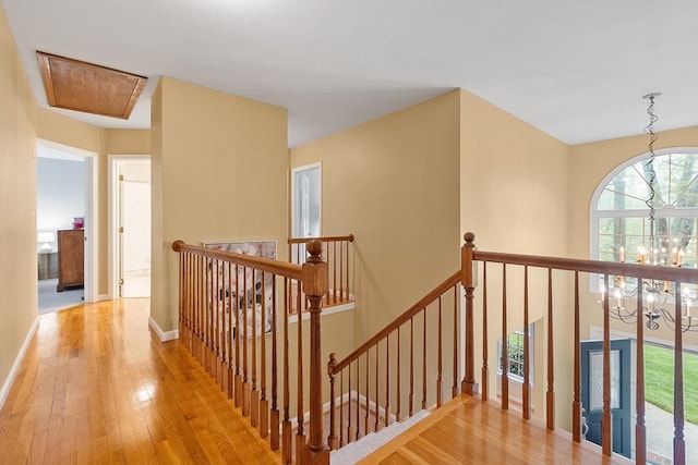 hallway featuring an upstairs landing, light wood finished floors, a chandelier, attic access, and baseboards