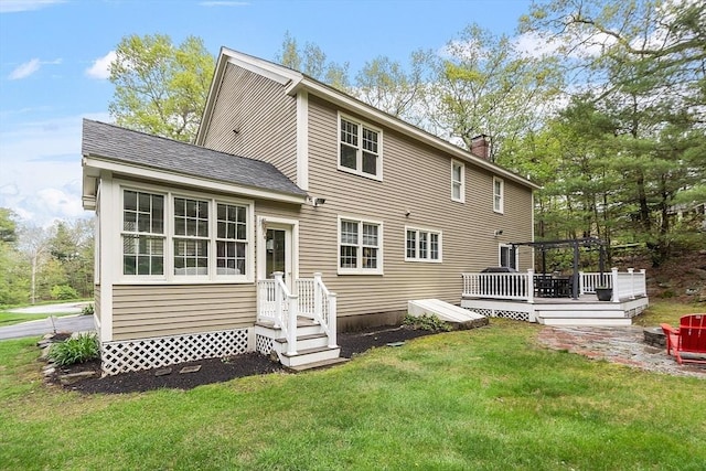 rear view of property featuring a deck, a chimney, a yard, and roof with shingles