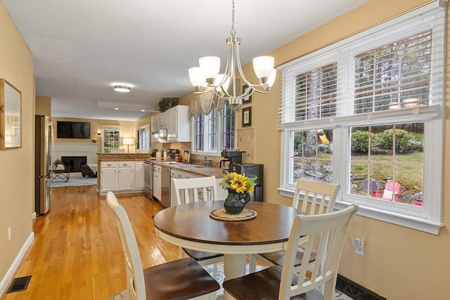 dining room featuring a chandelier, light wood-style floors, a glass covered fireplace, and baseboards