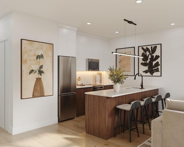 kitchen with white cabinets, freestanding refrigerator, light wood finished floors, modern cabinets, and a kitchen bar