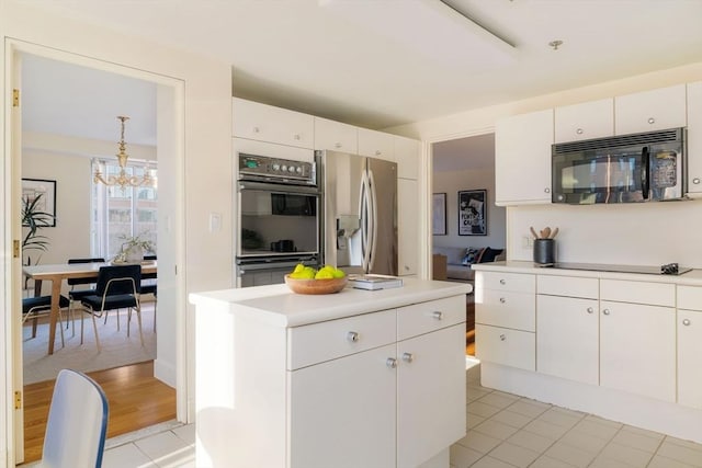 kitchen with a center island, light tile patterned floors, a notable chandelier, white cabinets, and black appliances