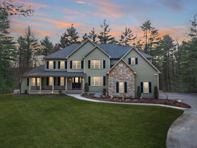 46 Mansfield Ave, Norton, MA 02766 - view of front facade featuring stone siding, a shingled roof, a yard, central AC unit, and a porch