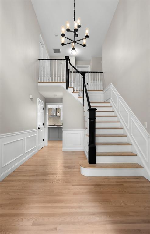46 Mansfield Ave, Norton, MA 02766 - staircase featuring wood finished floors, an inviting chandelier, a decorative wall, visible vents, and a towering ceiling