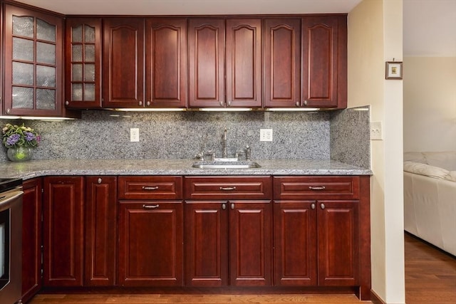 kitchen featuring reddish brown cabinets, backsplash, a sink, and wood finished floors