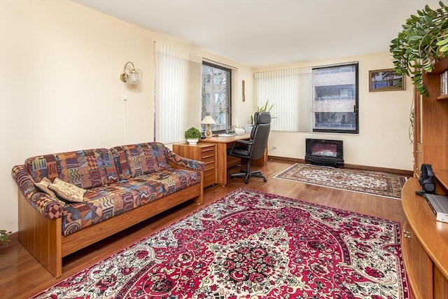 office area featuring baseboards, wood finished floors, and a glass covered fireplace