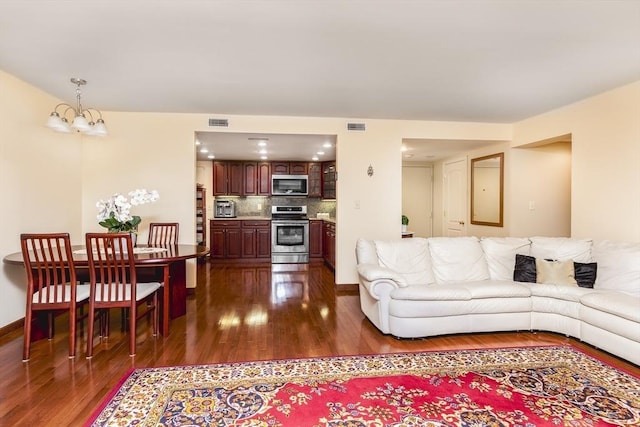 living room with baseboards, dark wood-type flooring, visible vents, and a notable chandelier