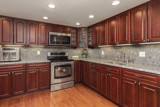 kitchen featuring appliances with stainless steel finishes, light wood-type flooring, a sink, and dark brown cabinets