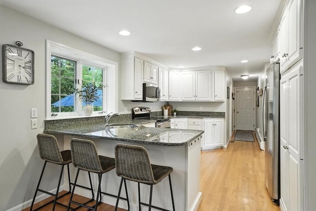 56 R F Higgins Dr, Norwell, MA 02061 - kitchen with appliances with stainless steel finishes, a peninsula, a kitchen bar, white cabinetry, and dark stone countertops