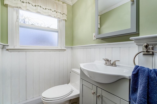 half bath featuring toilet, vanity, crown molding, and wainscoting