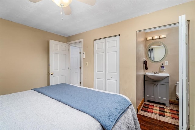 bedroom featuring a closet, dark wood-type flooring, a ceiling fan, a sink, and baseboards