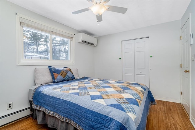 bedroom featuring ceiling fan, a baseboard radiator, wood finished floors, a closet, and a wall mounted air conditioner