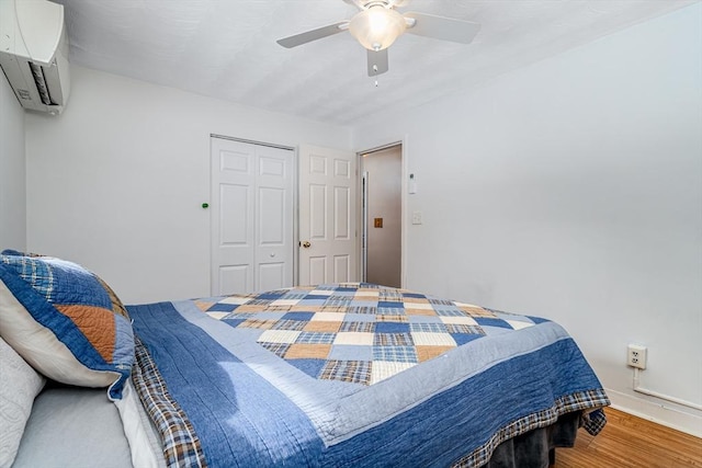 bedroom featuring a ceiling fan, a closet, a wall unit AC, and wood finished floors