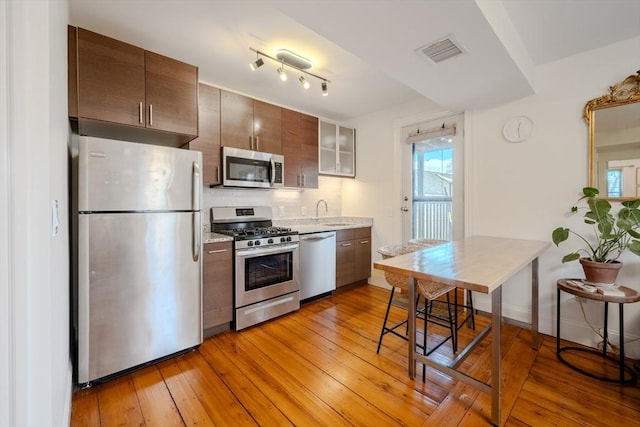 kitchen featuring light wood finished floors, visible vents, glass insert cabinets, appliances with stainless steel finishes, and a sink