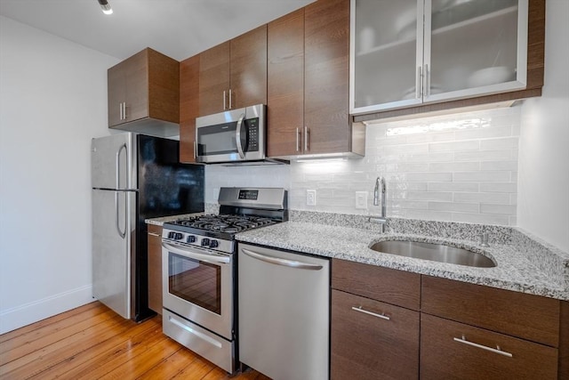 kitchen with stainless steel appliances, a sink, light wood-type flooring, backsplash, and glass insert cabinets