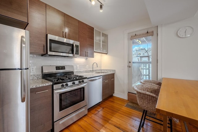 kitchen with light wood-style flooring, light stone counters, a sink, stainless steel appliances, and backsplash