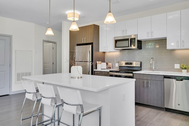 kitchen with decorative light fixtures, appliances with stainless steel finishes, hardwood / wood-style flooring, and tasteful backsplash