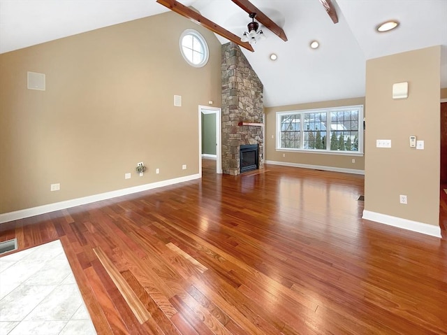 unfurnished living room featuring a stone fireplace, hardwood / wood-style floors, high vaulted ceiling, beamed ceiling, and ceiling fan