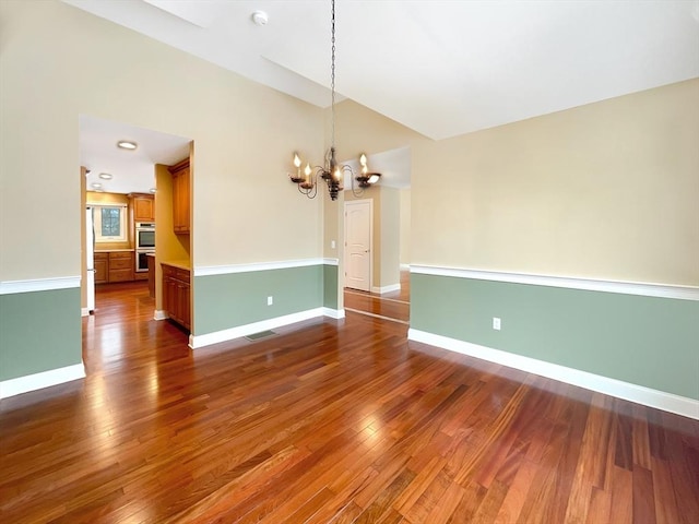 empty room featuring vaulted ceiling, dark hardwood / wood-style floors, and an inviting chandelier