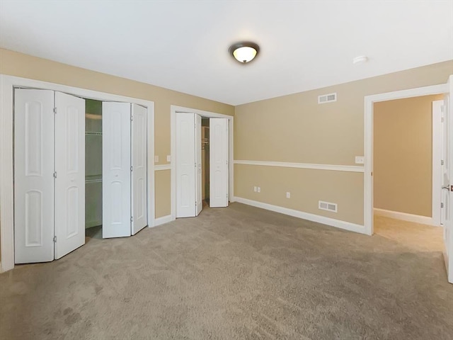 unfurnished bedroom with light colored carpet and two closets