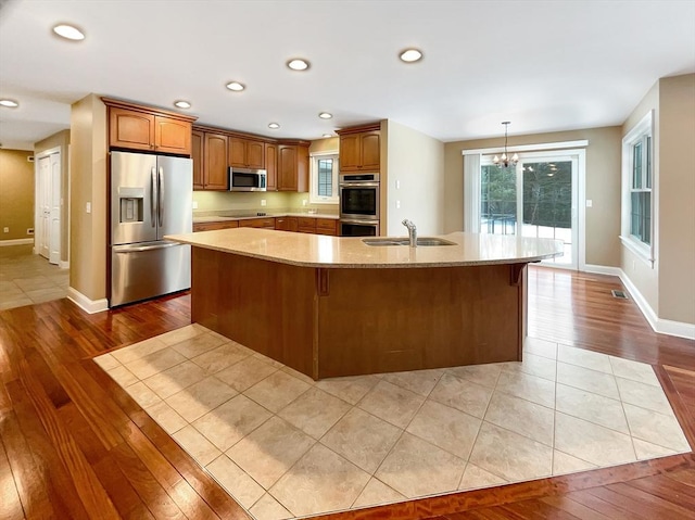 kitchen featuring sink, light hardwood / wood-style flooring, appliances with stainless steel finishes, light stone countertops, and a kitchen island with sink